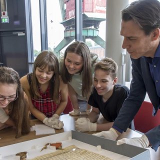 Schülerinnen und Schüler betrachten gemeinsam mit ihrem Lehrer eine Urkunde mit zwei Siegeln. 